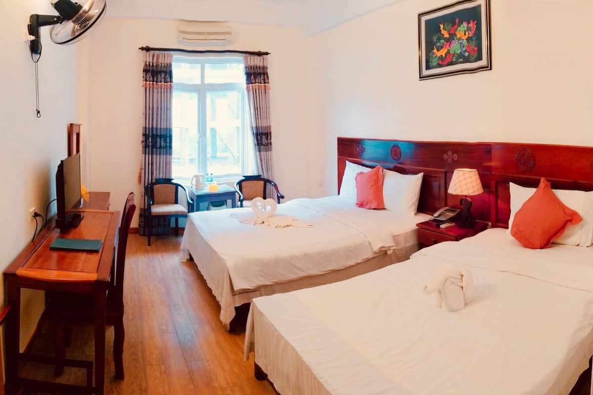 A hotel room with two beds, a desk, a chair, a TV, and a window with curtains.