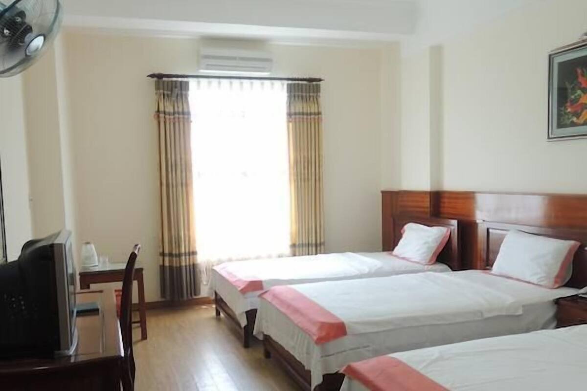 A hotel room with two single beds, a desk with a chair, a television, and a window with curtains.