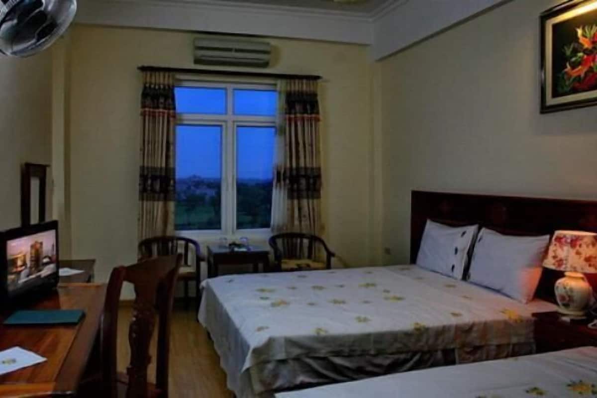 A hotel room with a bed, a desk with a computer, a chair, and a window with curtains.