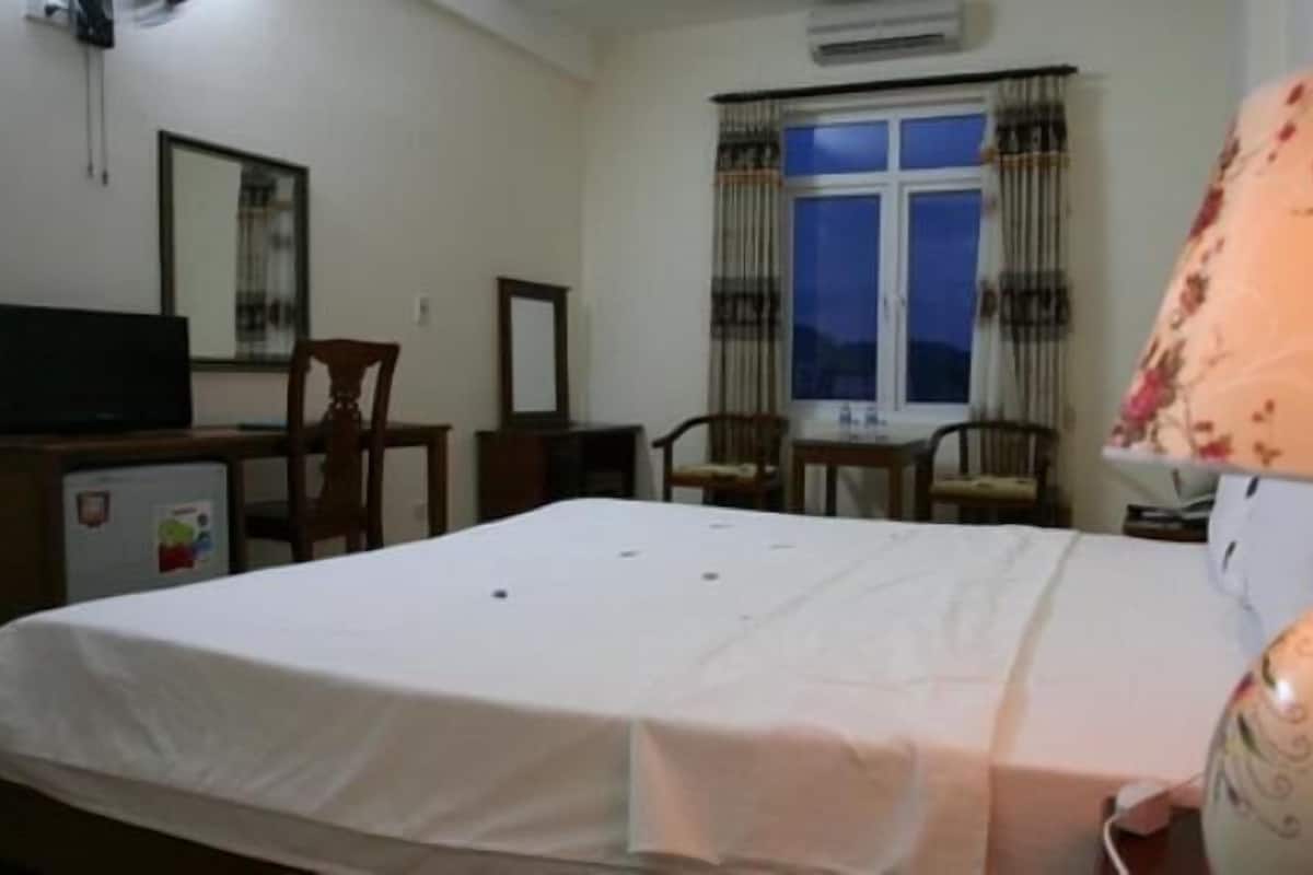 A bedroom with a bed, a desk with a computer, a chair, a lamp, and a window with curtains.