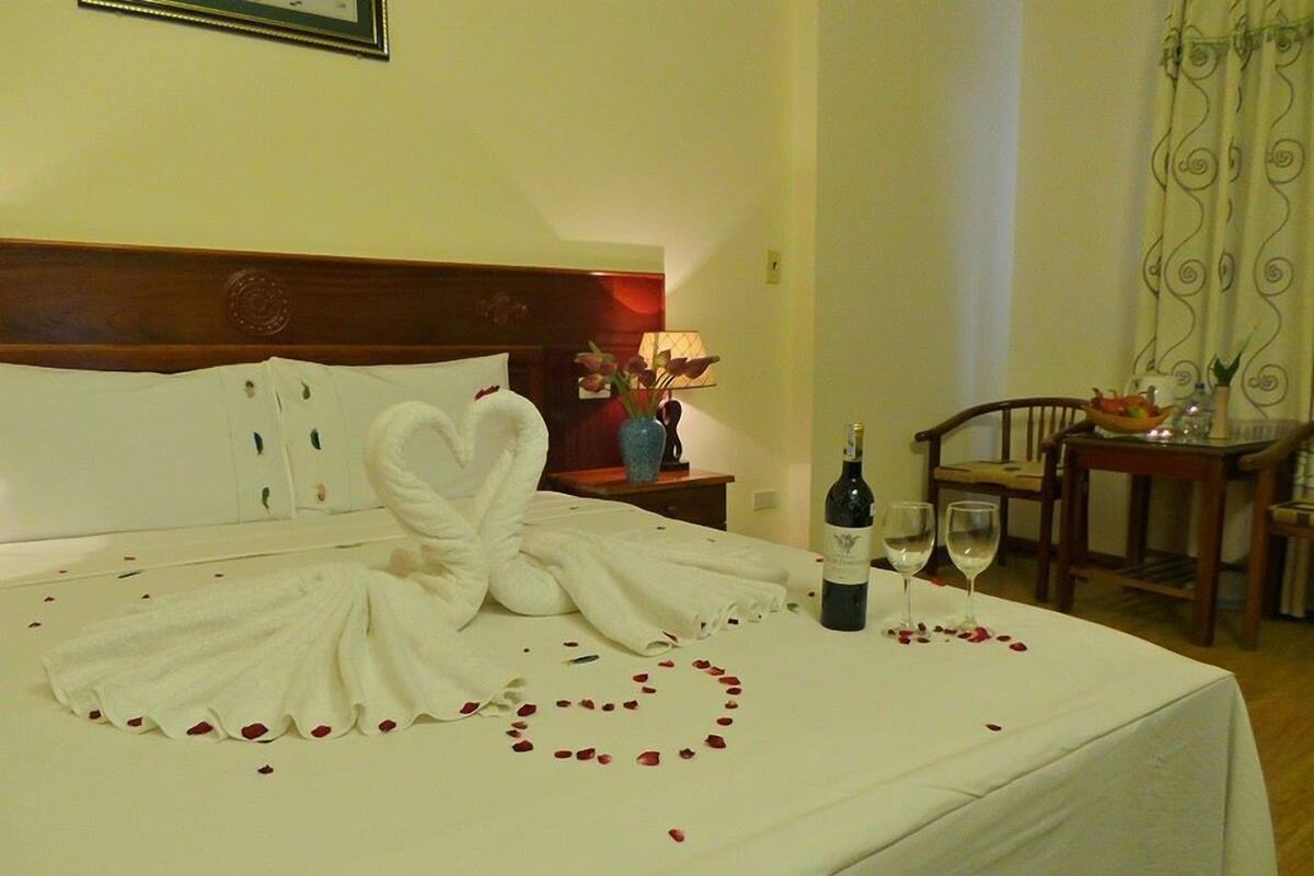 A hotel room with a bed, a bottle of wine, and a glass on the bedside table.