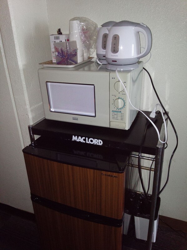 A microwave and coffee maker on a black countertop with a wooden cabinet below. - Hotel Unicorn (Nagano)