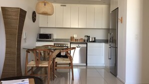 Une cuisine moderne avec des meubles blancs, des appareils en acier inoxydable et un coin repas comprenant des chaises en bois et une table en verre.