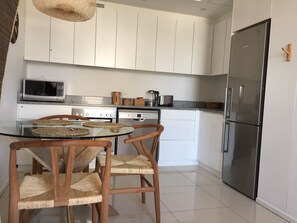 A modern kitchen with white cabinets, stainless steel appliances, and a glass dining table with woven chairs.