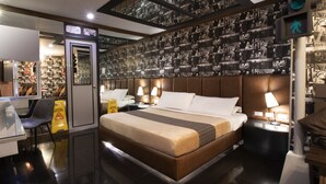 A modern hotel room with a large bed, bedside tables with lamps, a desk with a chair, and a wall decorated with black and white photographs. - Victoria Court Canley - Pasig (Pasig)