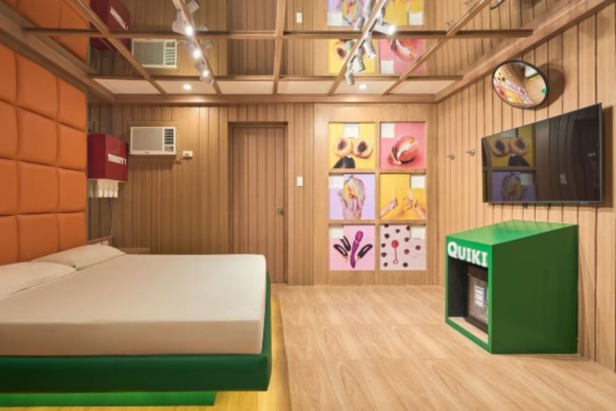 A hotel room with a bed, a green storage unit, a TV, and a wooden ceiling with artwork.