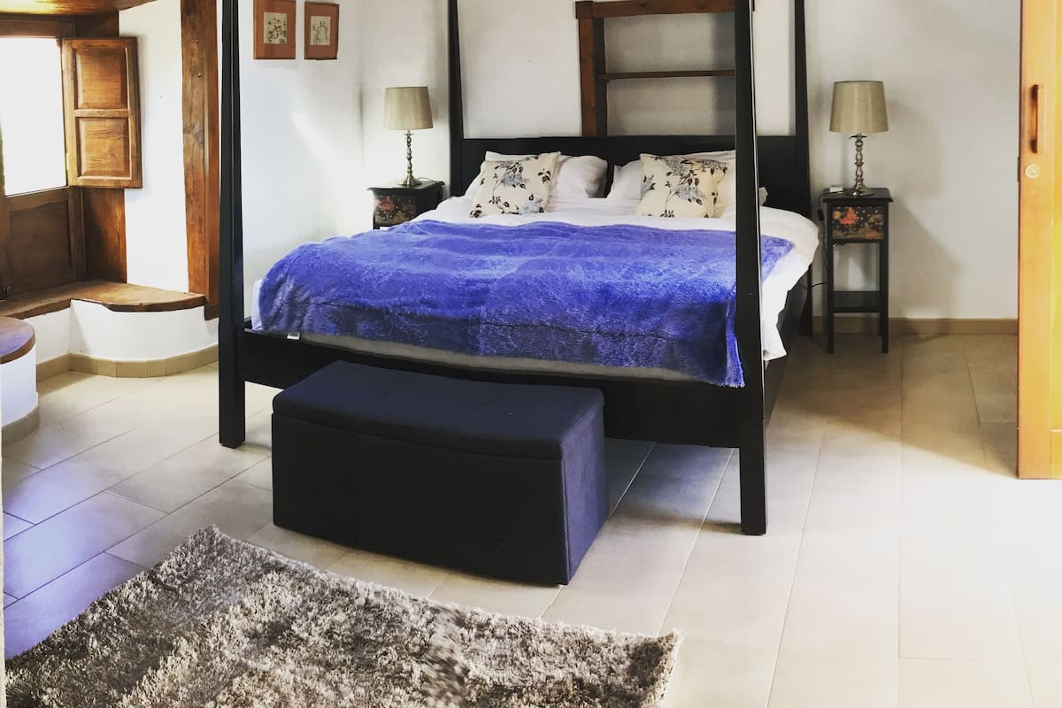 Ein Bett mit Baldachin, mit blauer Decke, zwei Nachttische mit Lampen, eine Holzdecke und ein kleiner Teppich auf dem Boden.