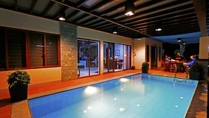 En inomhuspool med väggar av genomskinligt glas, en vägg som är accentuerad med sten och en modern takdesign.