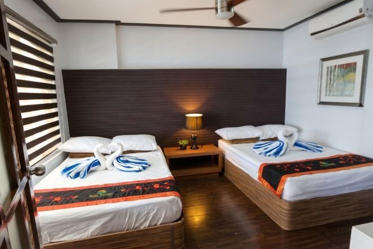 A hotel room with two single beds, a bedside table with a lamp, and a ceiling fan.