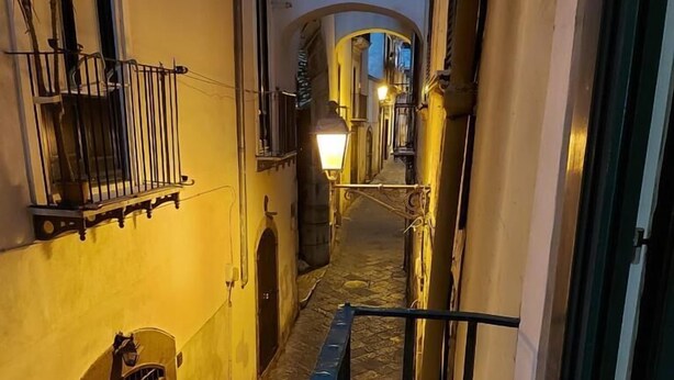 Une ruelle étroite dallée de pierres, avec des portes en arc de cercle et un garde-corps bleu.