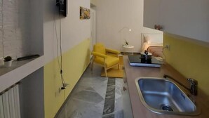 Une cuisine étroite avec un sol en marbre, une chaise jaune, un évier et un téléviseur fixé au mur.