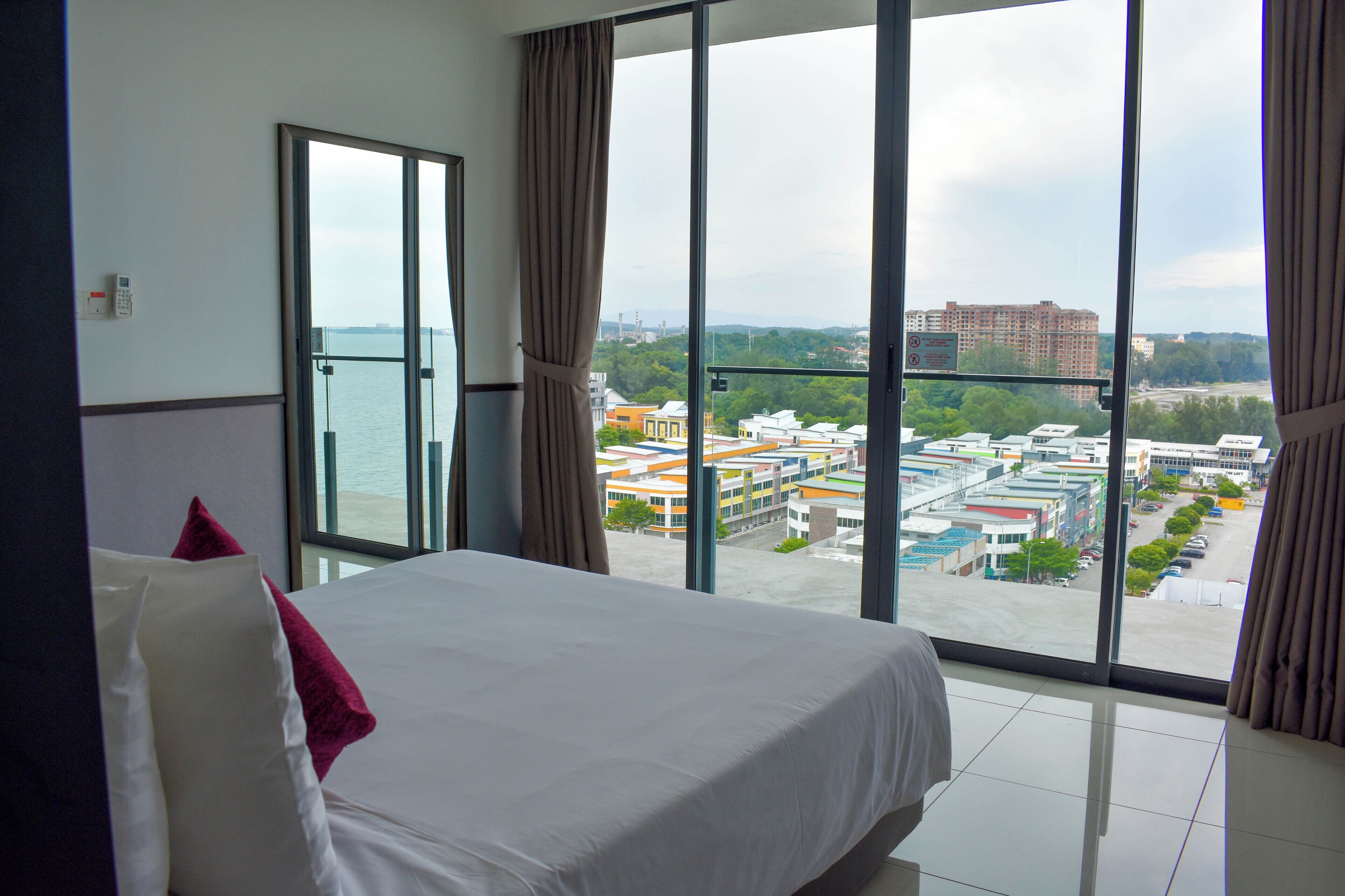 Habitación de hotel con una cama grande, vista a un paisaje urbano y balcón con vista al mar.