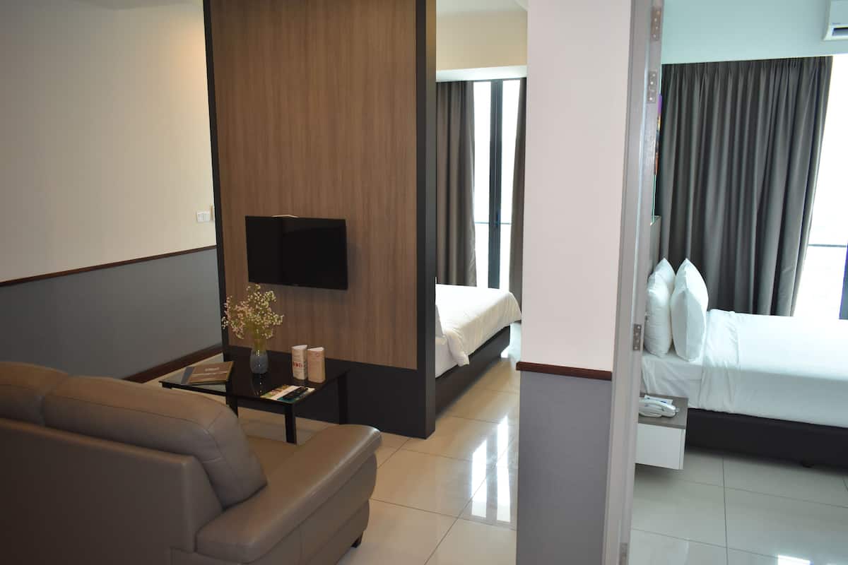A hotel room with a sofa, a TV, a bedside table with a vase, and a bed with pillows.