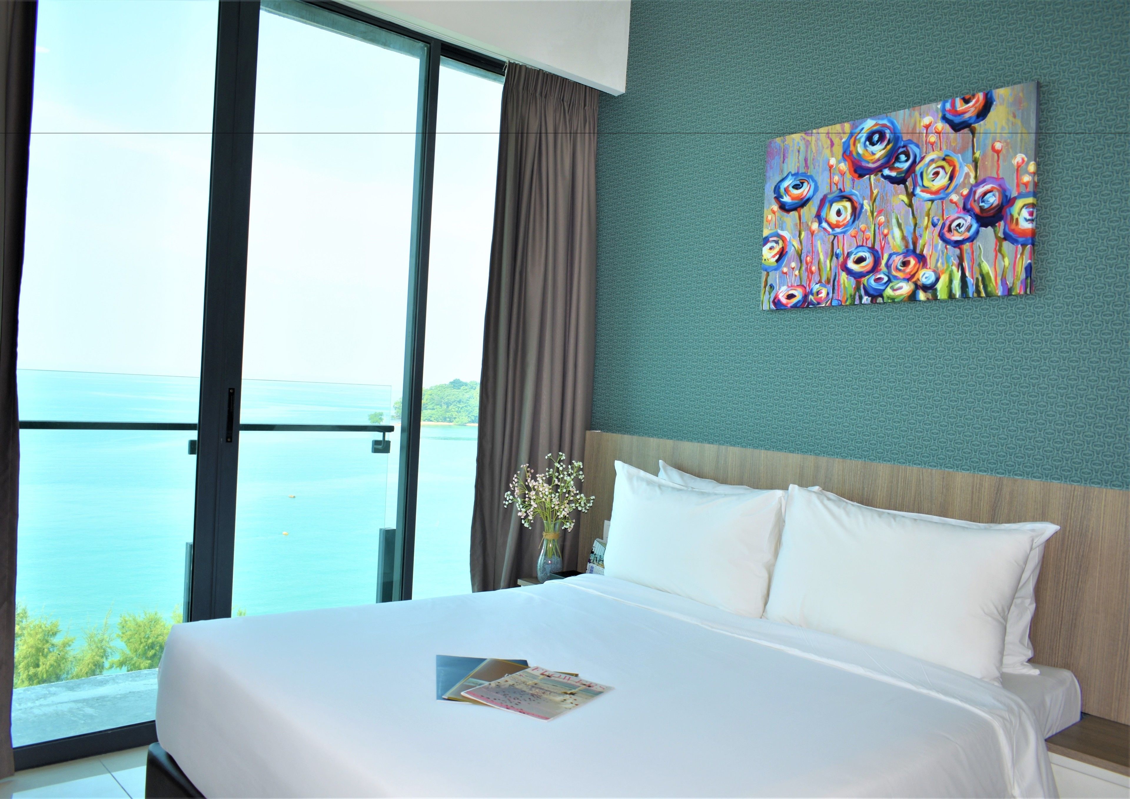 A hotel room with a large bed, a painting on the wall, and a view of the sea through the window.