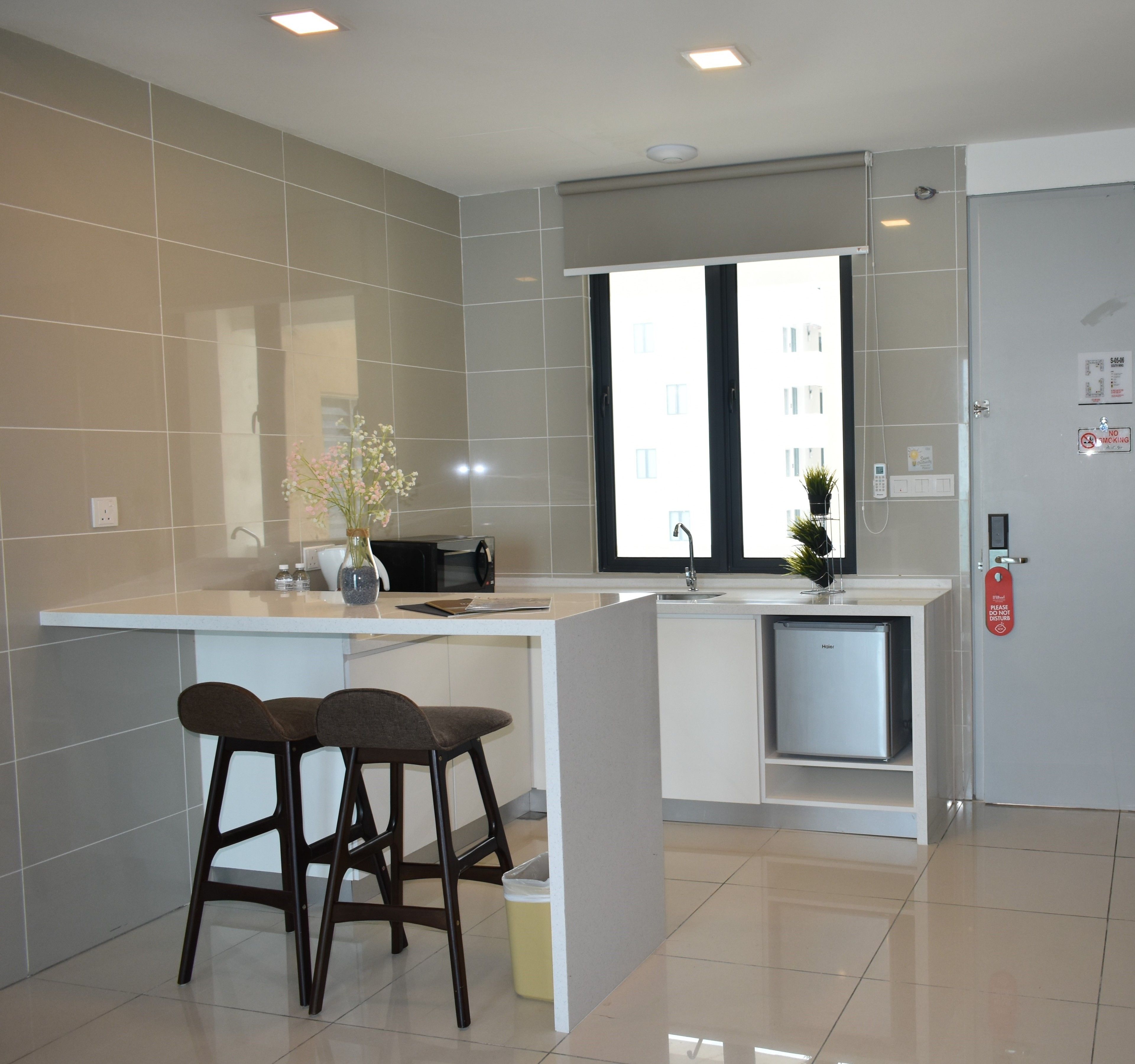 A modern kitchen with a built-in island, two bar stools, a refrigerator, and a window with a view of buildings.