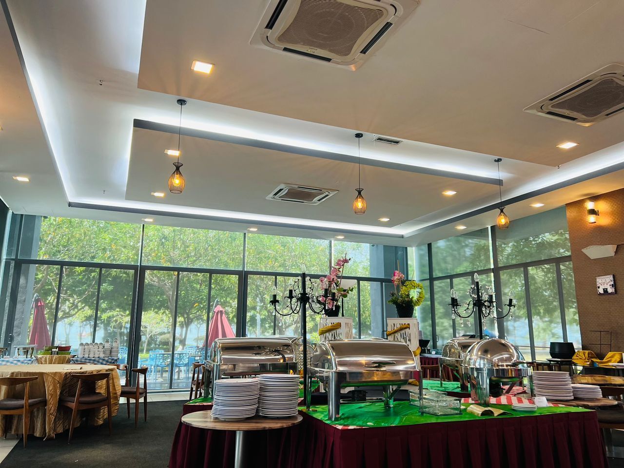 A dining area with buffet setup, large windows, and ceiling lights.