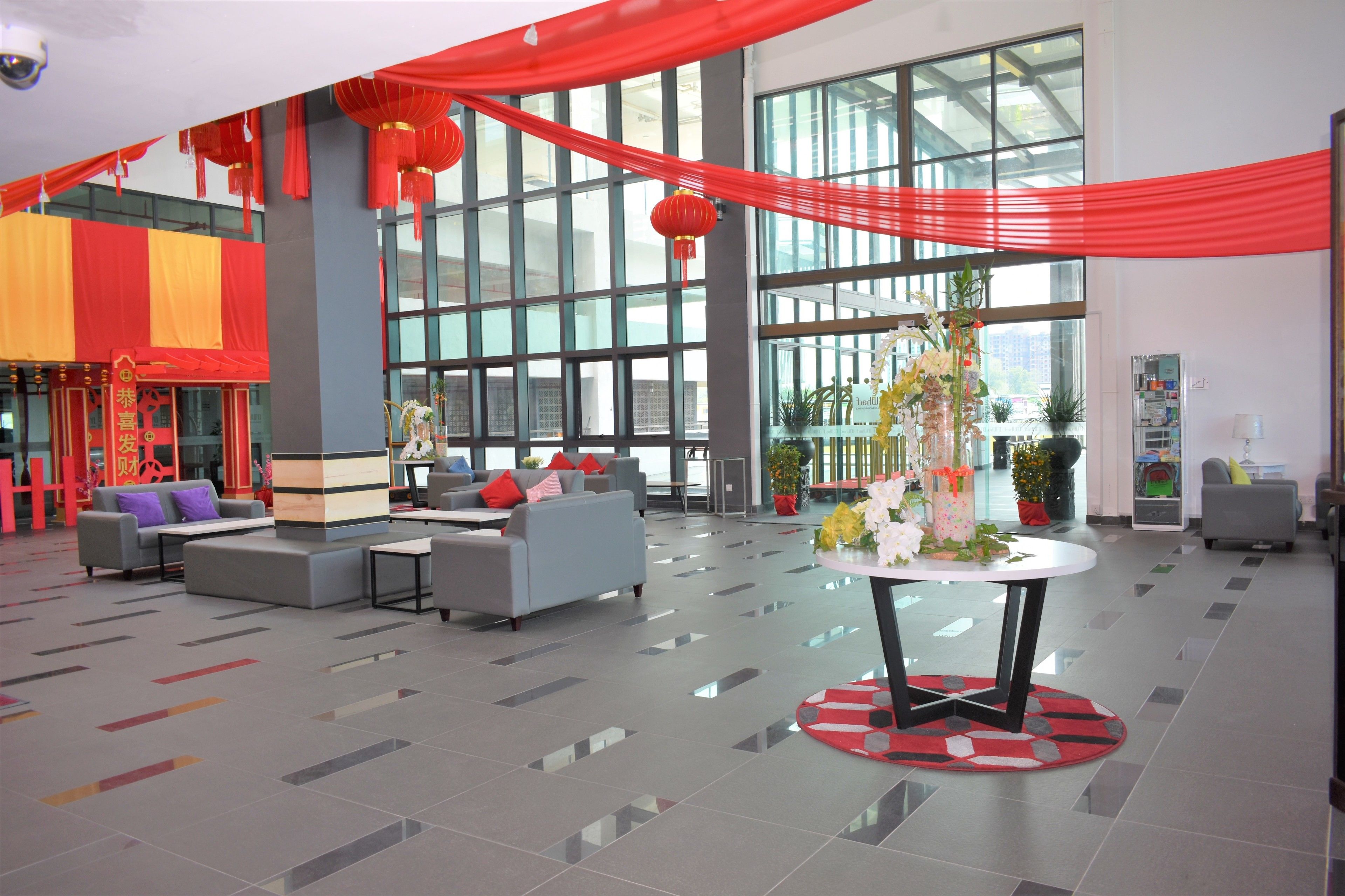 A spacious lobby with modern furniture, large windows, and red decorative elements.