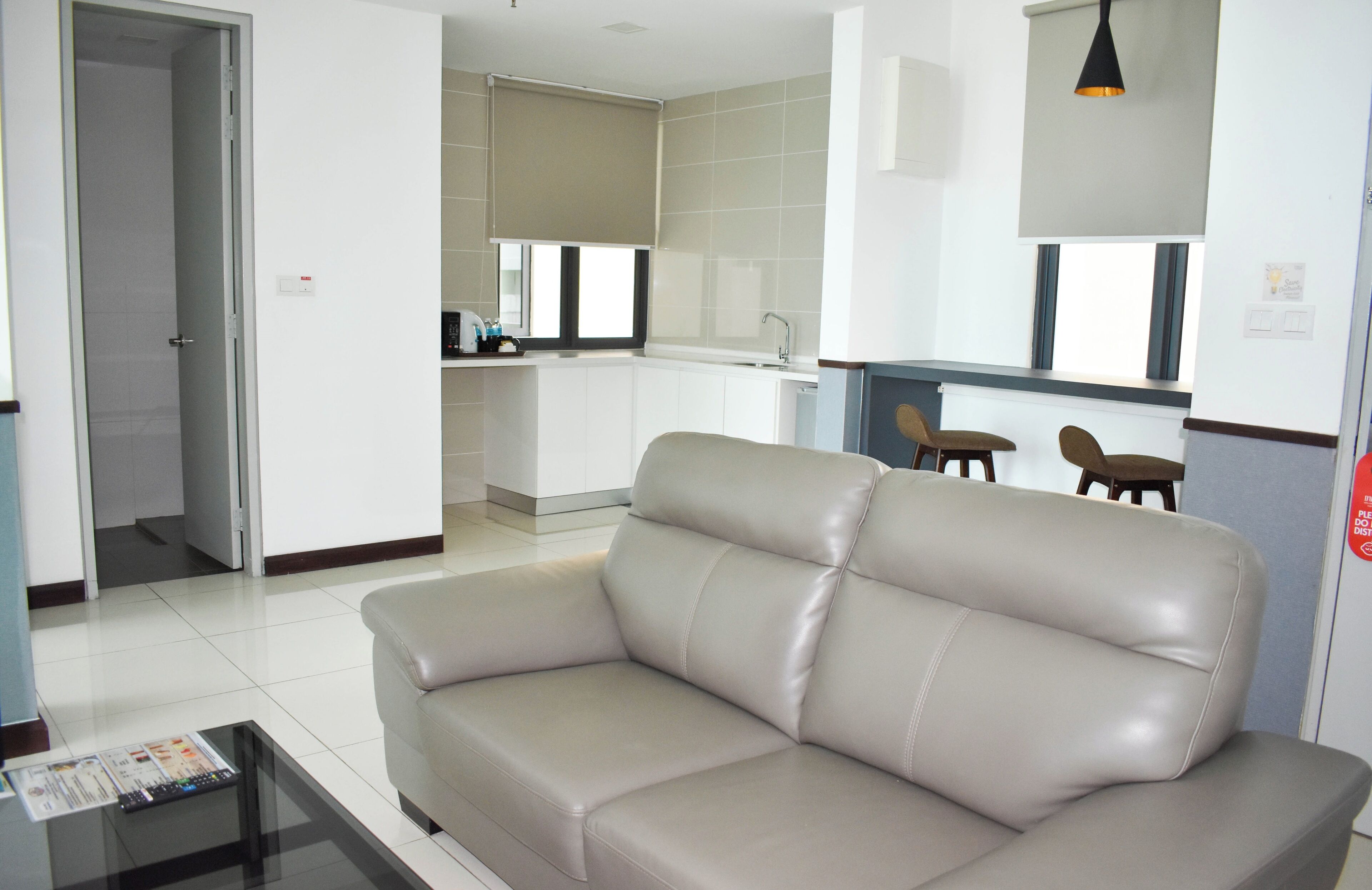 Una sala de estar moderna con un sofá color beige, una mesa de centro de cristal y una zona de cocina al fondo.