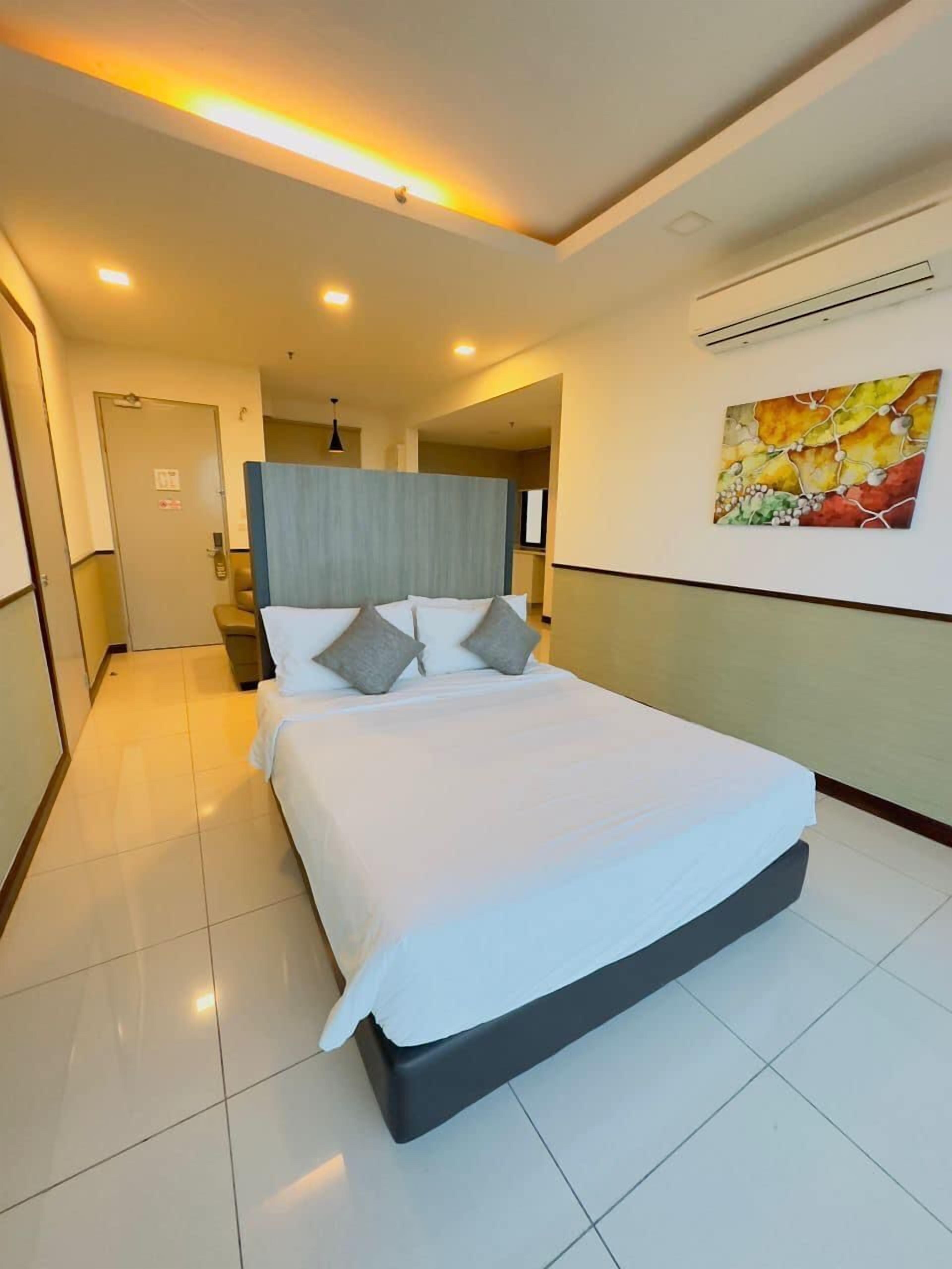 A hotel room with a large bed, a headboard, a flat-screen TV, and a painting on the wall.