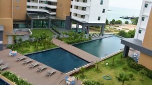 A modern hotel with a swimming pool, lounge chairs, and a view of the sea. - D'Wharf Hotel & Serviced Residence (Port Dickson)