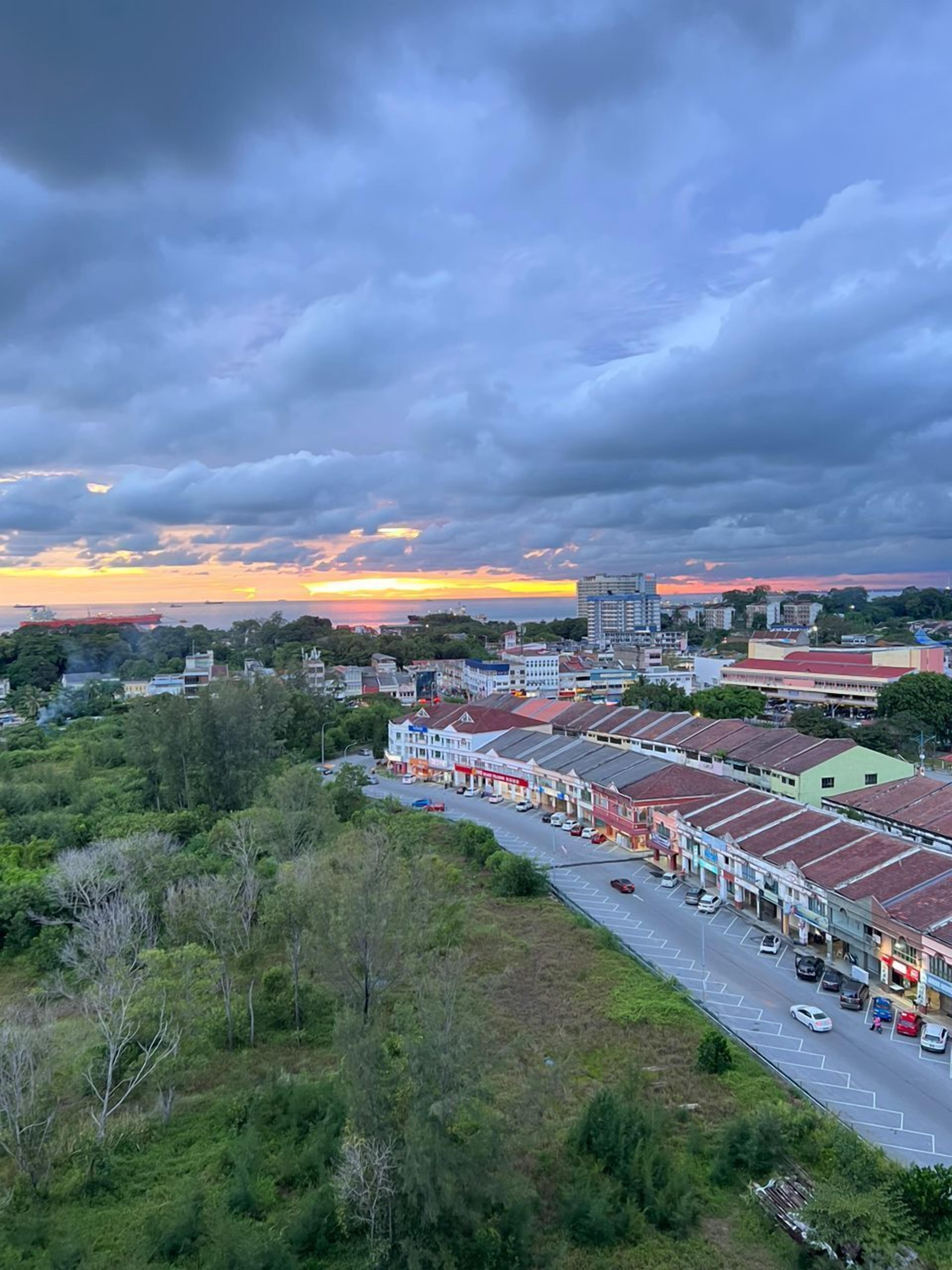 Un pueblo costero con una amplia avenida, edificios y un atardecer.