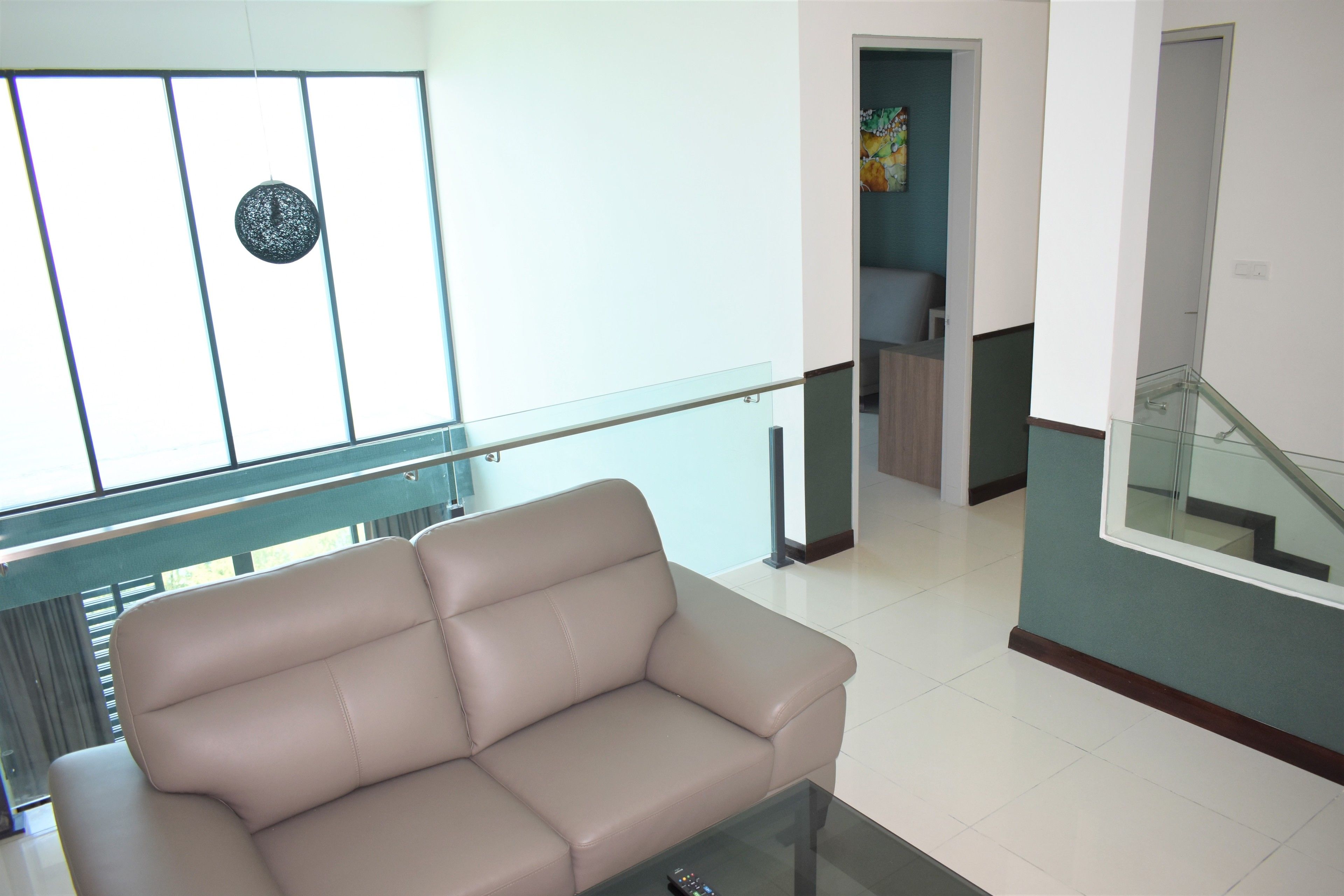 Uma sala de estar moderna com um sofá bege, uma mesa de centro de vidro e vista para uma escada e corredor.
