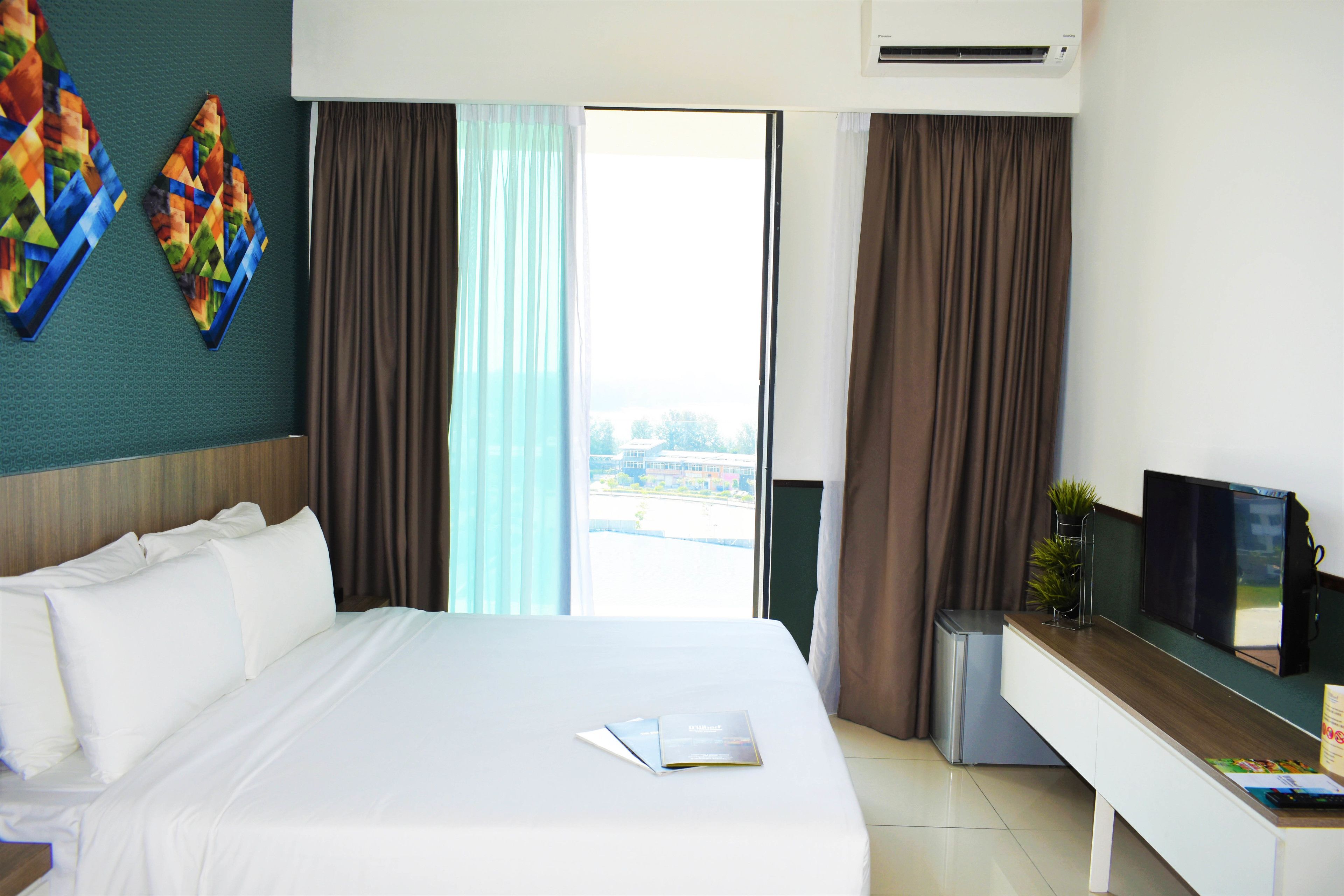A hotel room with a bed, a desk, a television, and a view of the city.