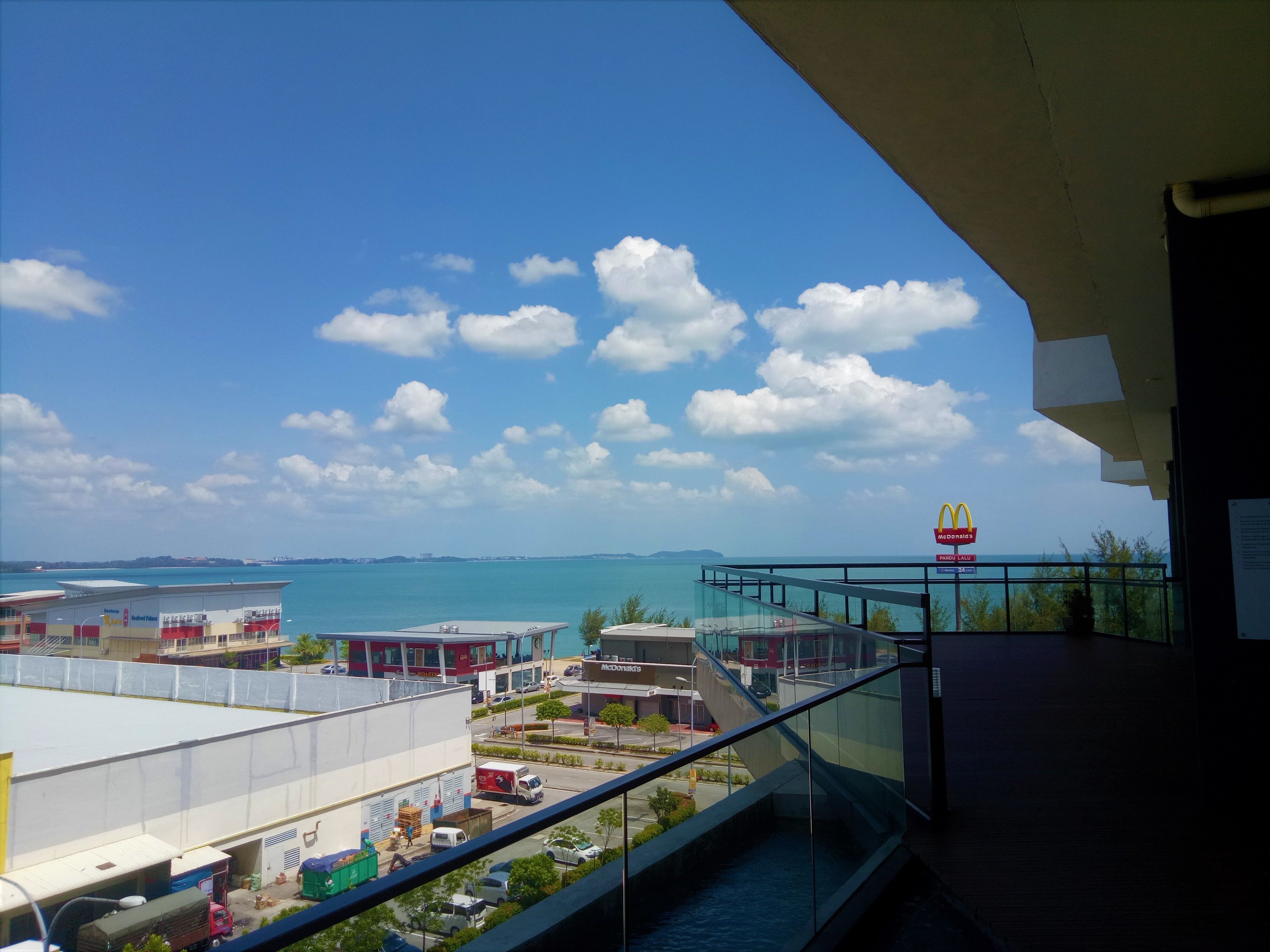A view from a balcony overlooking a commercial area with a clear sky, a body of water, and a McDonald's restaurant.