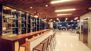 Zona de bar moderna con techo de madera, estanterías de cristal y mostrador con taburetes.