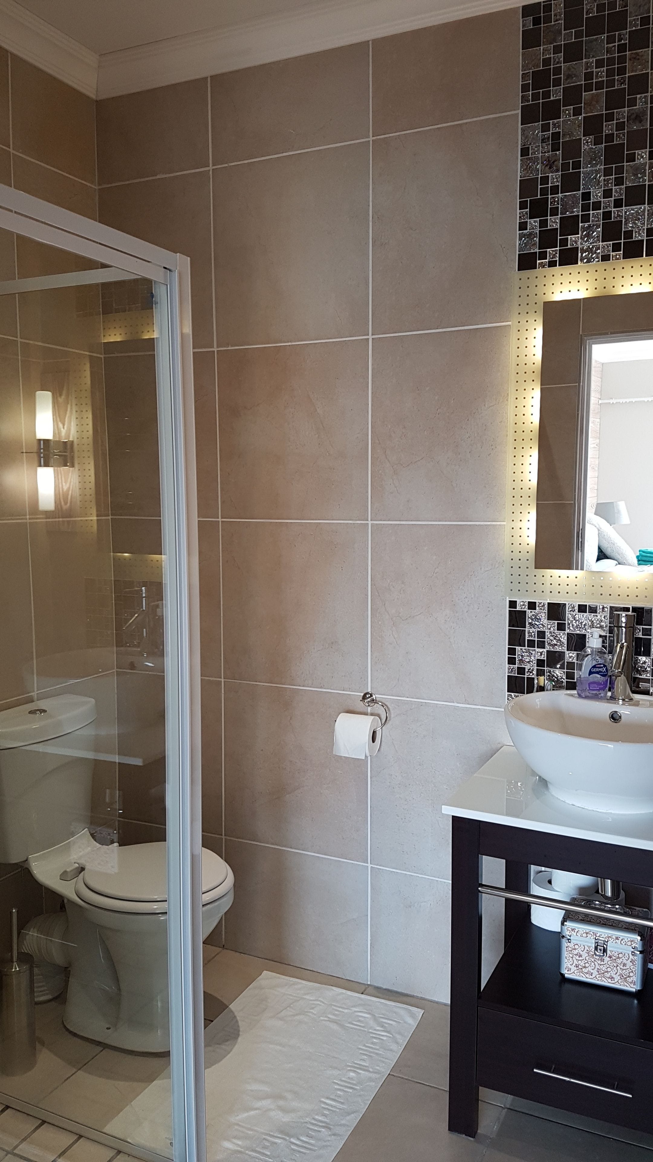A bathroom with a glass shower enclosure, a toilet, a sink with a mirror, and tiled walls.
