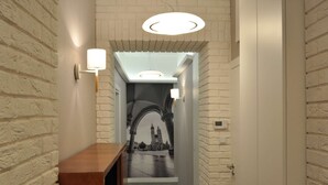 Un pasillo con paredes de ladrillo blanco, un banco de madera y un cuadro enmarcado con una vista urbana.