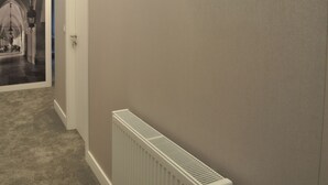 Un pasillo con un radiador, una puerta y vistas a una habitación con candelabro.