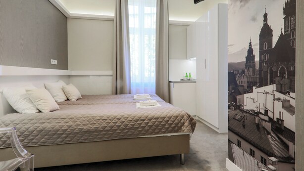 Habitación de hotel con cama, escritorio, silla, ventana con cortinas y televisor montado en la pared.