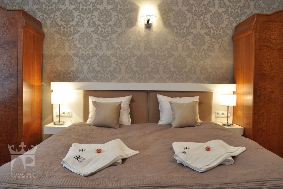 A neatly made double bed with two pillows, two bedside lamps, and two folded towels on the bed.