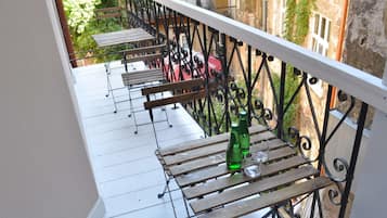 Ein Balkon mit Holztischen und -stühlen, einem Metallgeländer sowie einer Flasche und einem Glas auf einem der Tische.