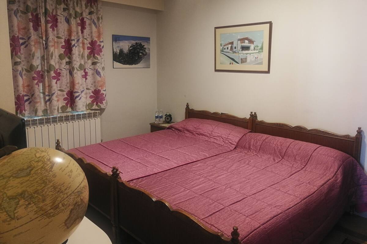 Un dormitorio con una cama de madera, un globo terráqueo, cortinas con estampado floral y dos cuadros en la pared.