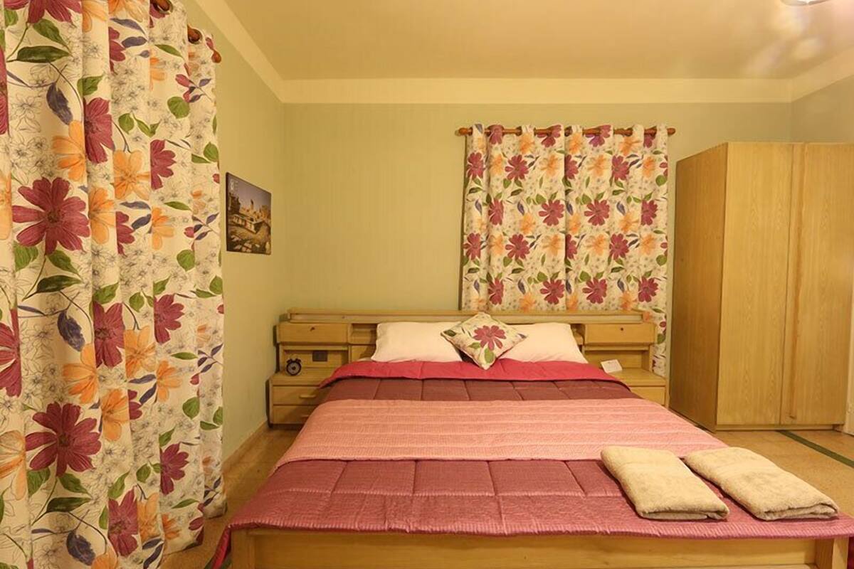 Un dormitorio con una cama de madera, cortinas florales, una mesita de noche y un armario.