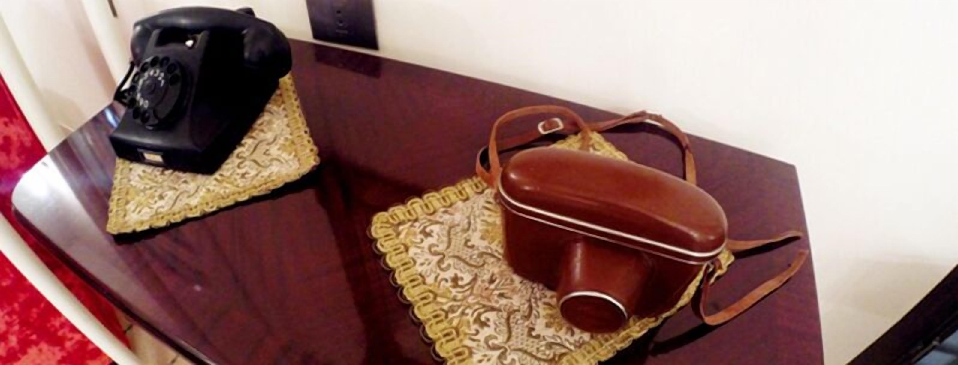 A wooden table with a vintage rotary phone and a brown leather handbag on a decorative placemat.