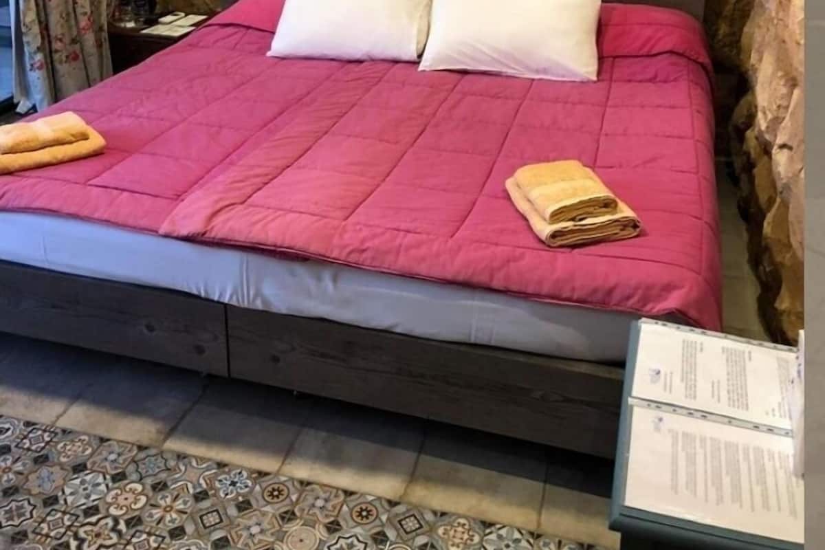 Una cama con un edredón rosa, dos almohadas y una toalla doblada a cada lado.