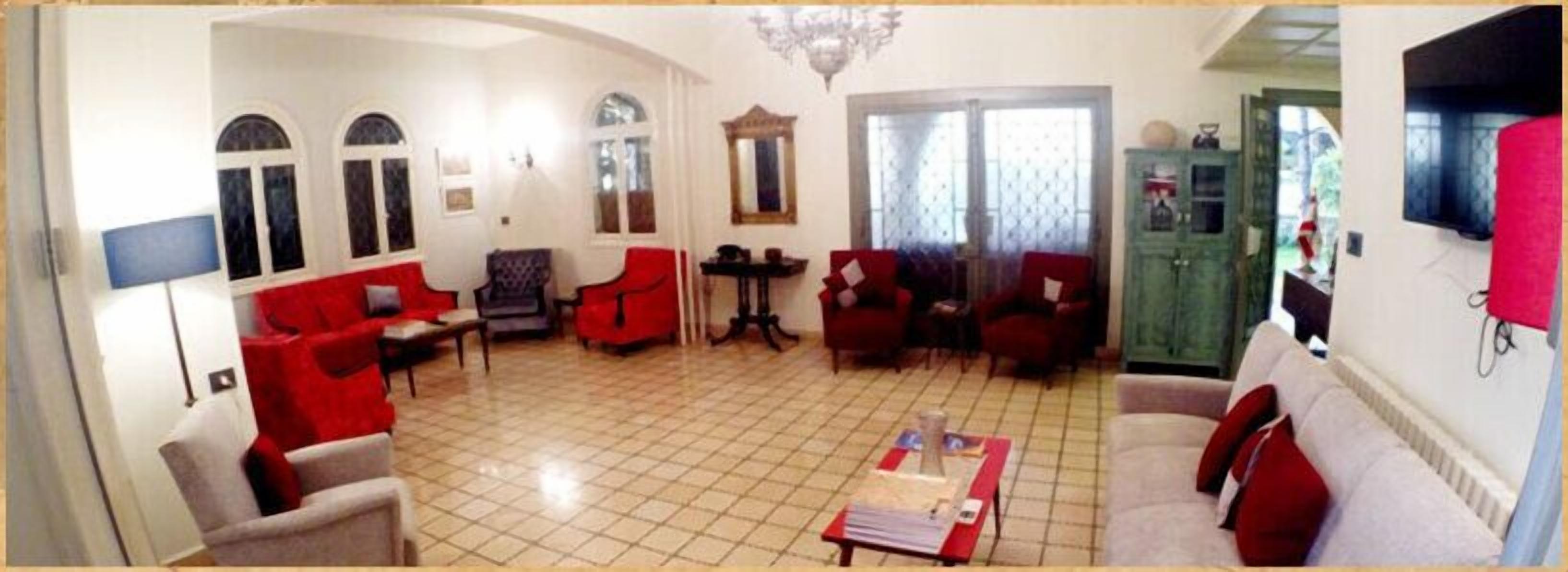 A spacious living room with red and white furniture, a chandelier, and a television.