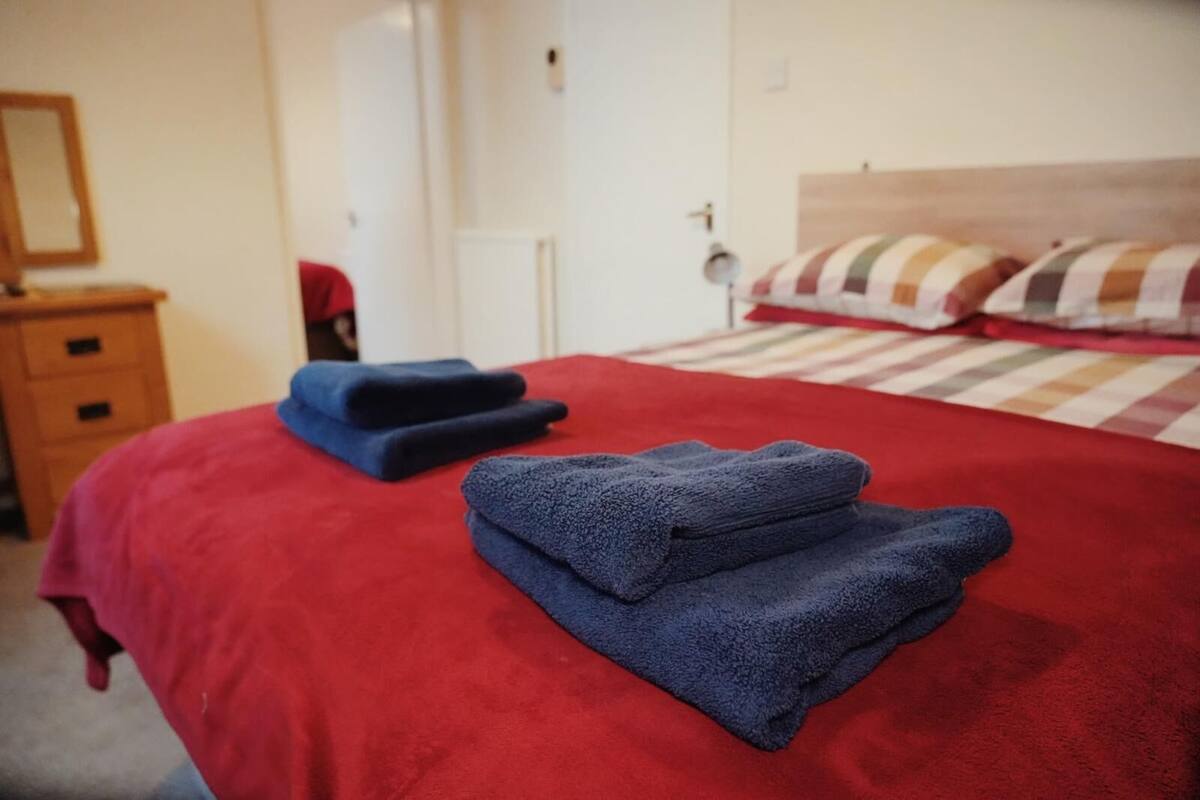 A neatly made bed with a red bedspread and two folded blue towels.