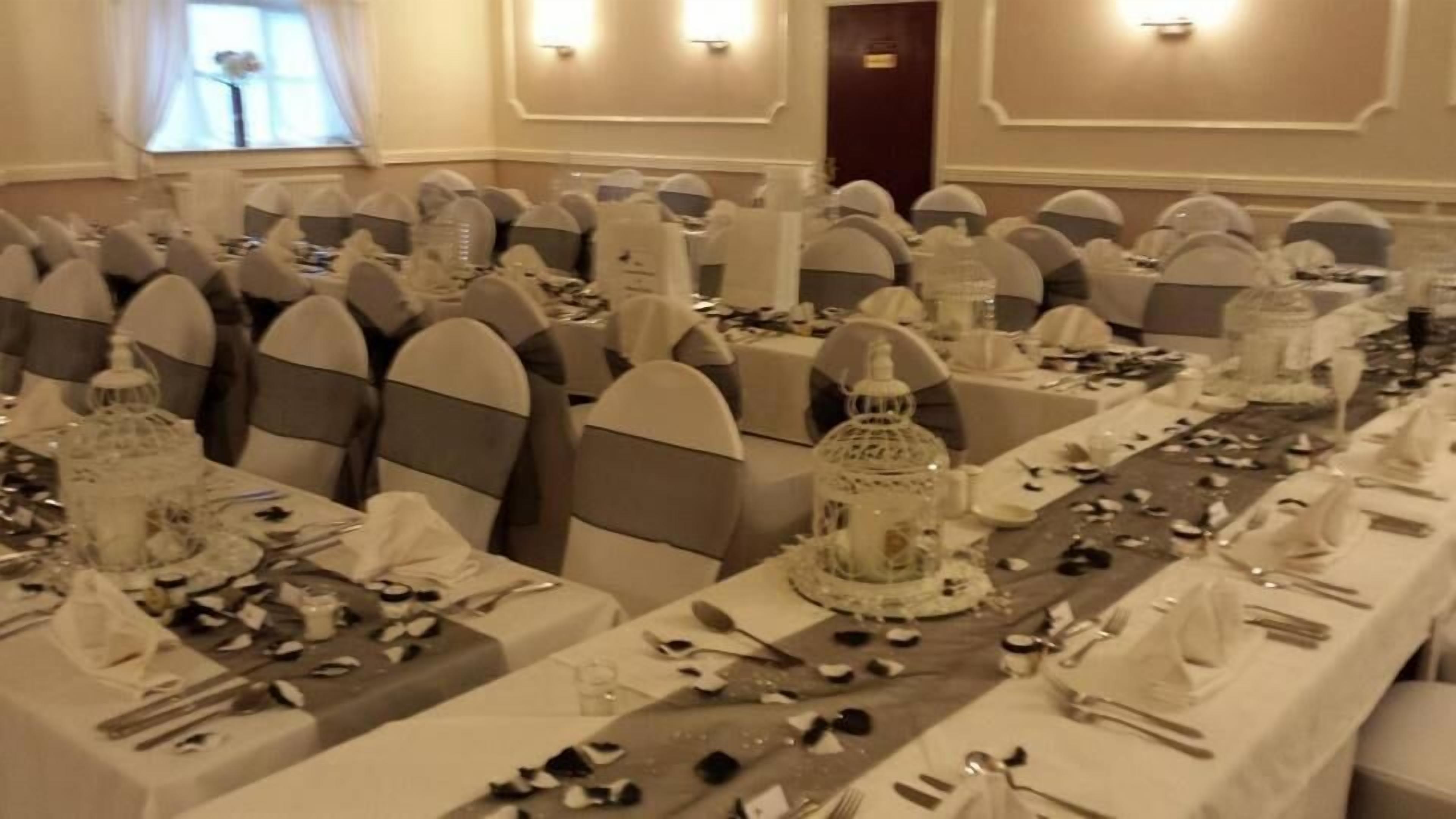 Un salón de banquetes con largas mesas dispuestas para un evento formal, con manteles blancos, copas y cubertería.