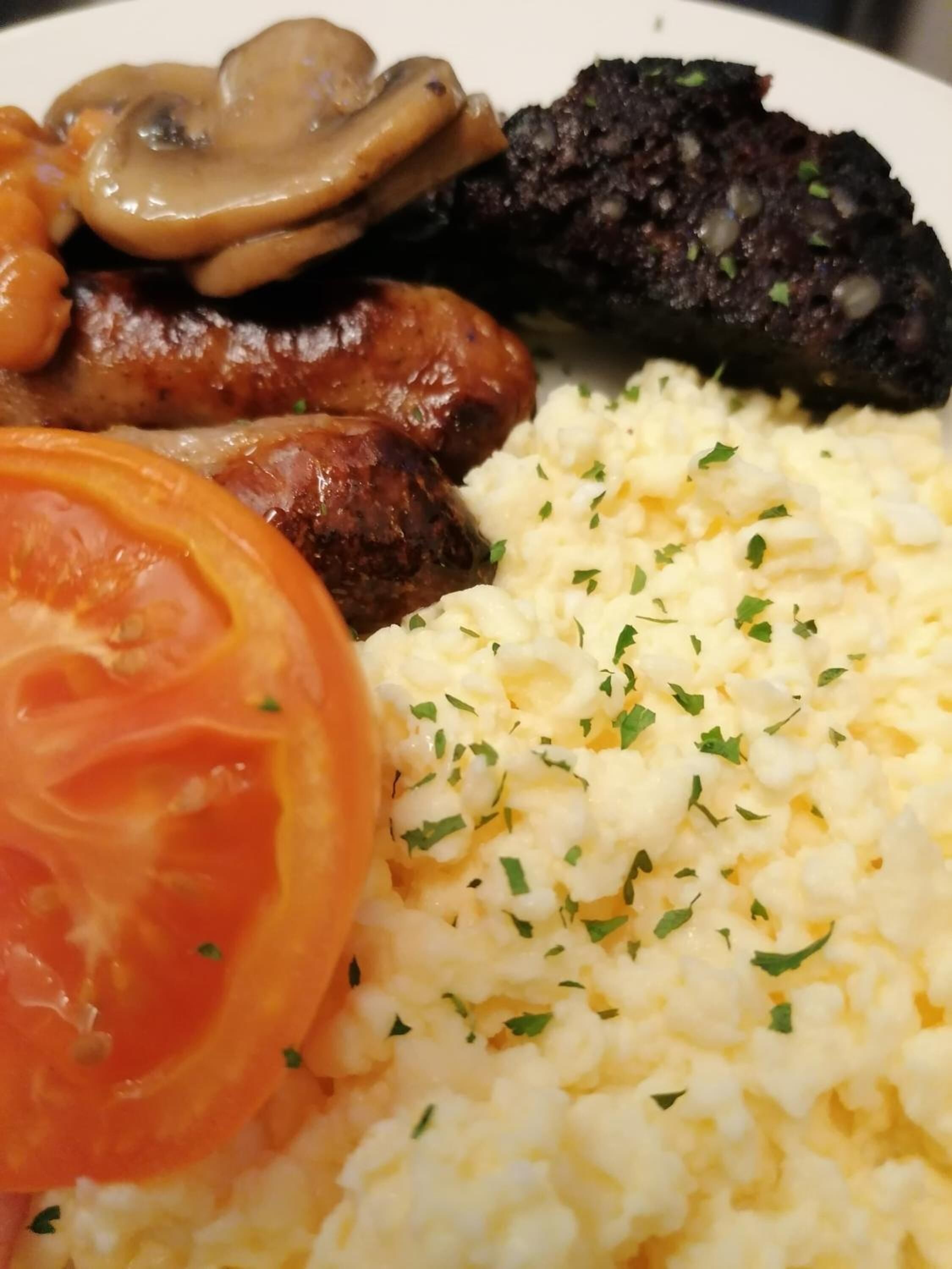 A plate with scrambled eggs, sausages, mushrooms, and a slice of tomato.