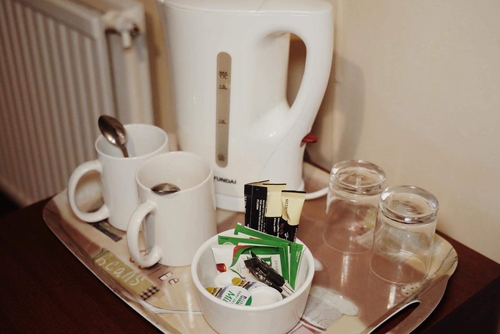 A tray with a coffee maker, two mugs, a cup of coffee, a box of coffee pods, and two glasses.