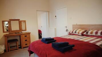 Un dormitorio con cama, escritorio, silla, espejo y puerta.