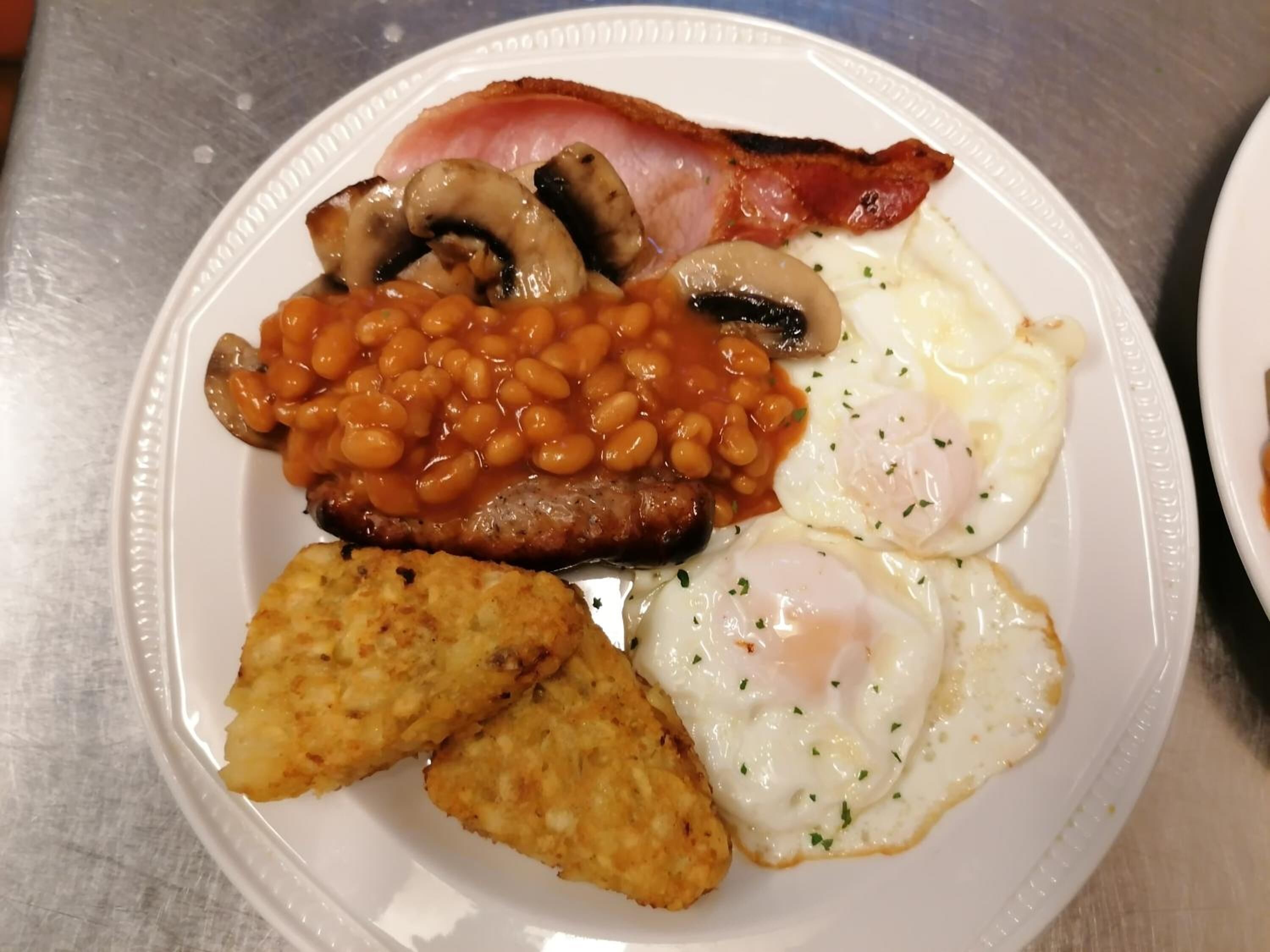 A plate of breakfast food including bacon, eggs, beans, mushrooms, sausages, and hash browns.