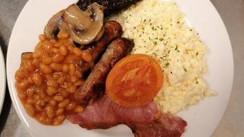 Un plato con frijoles, salchichas, champiñones, tocino, huevos revueltos y tomate.