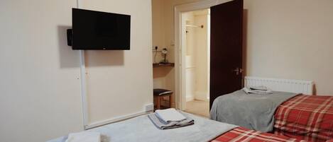 Un dormitorio con dos camas, un televisor montado en la pared y una puerta que da a un baño.