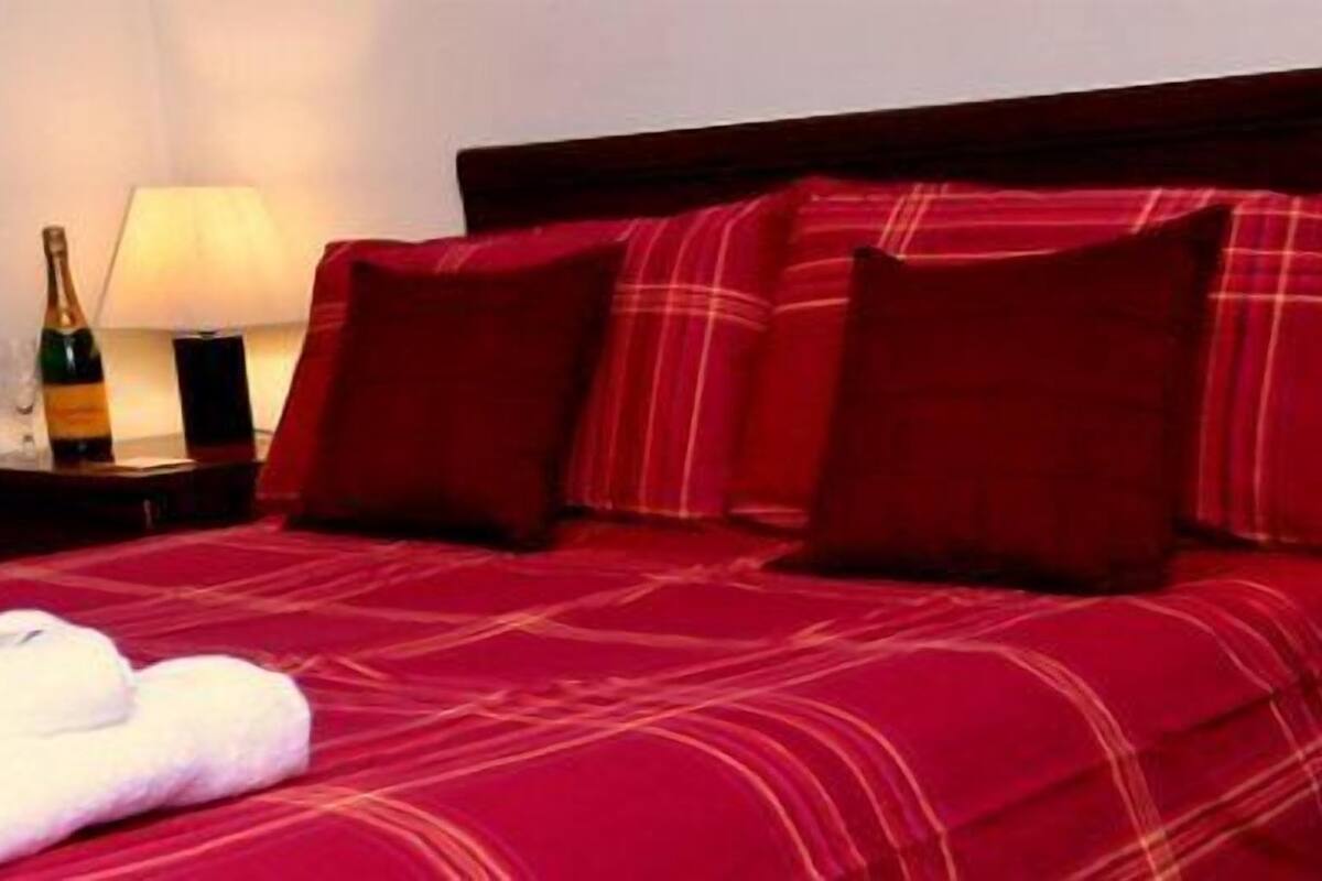 A hotel room with a red bedspread, pillows, a white towel, and two bedside lamps.