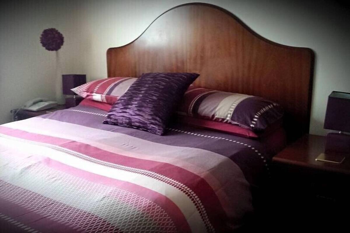 A bed with a wooden headboard, multiple pillows, a striped bedspread, and bedside lamps.